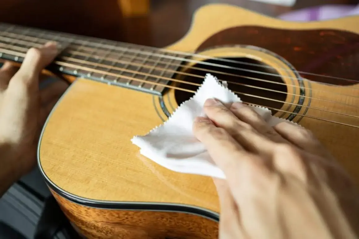 Mani che puliscono la chitarra classica con un panno bianco, un gesto essenziale per la cura dello strumento.