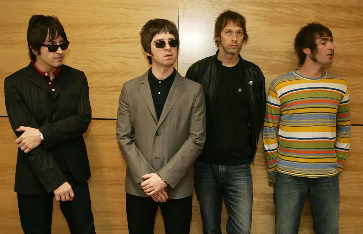 I quattro membri degli Oasis, con i loro look iconici, sembrano pronti per un concerto, un'istantanea degli anni '90.