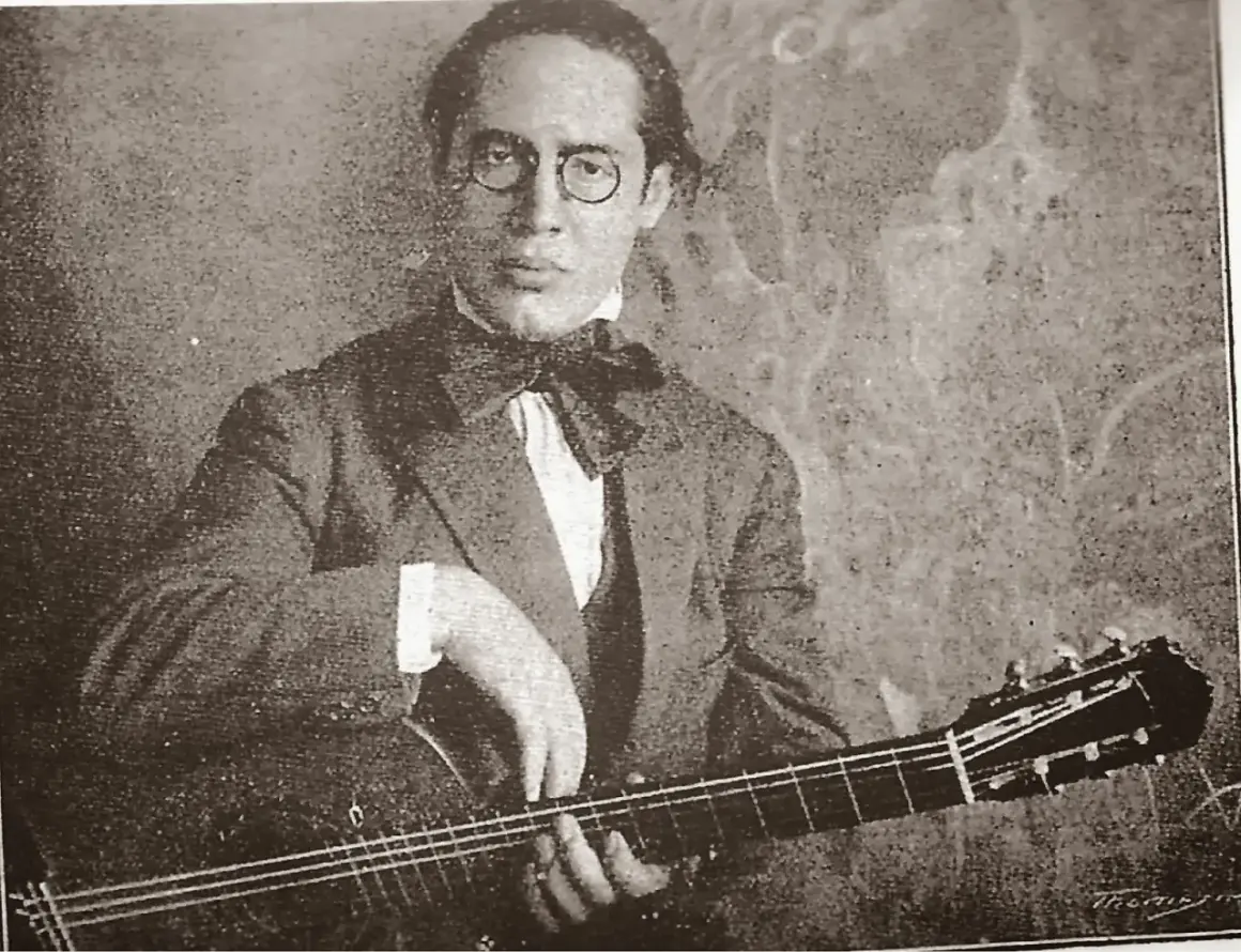 Ritratto di Andrés Segovia, chitarrista, con occhiali rotondi e papillon, mentre suona la sua chitarra.