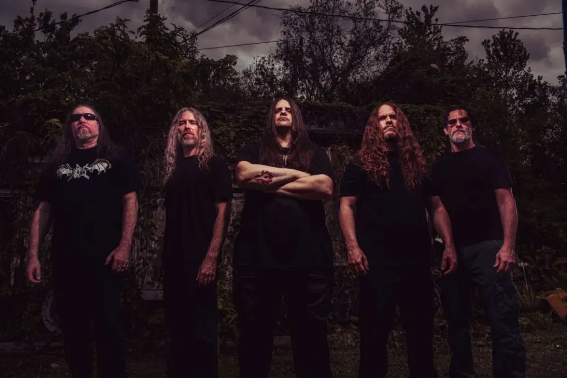 I membri dei Cannibal Corpse posano in un ambiente esterno cupo, con alberi e cielo nuvoloso sullo sfondo.