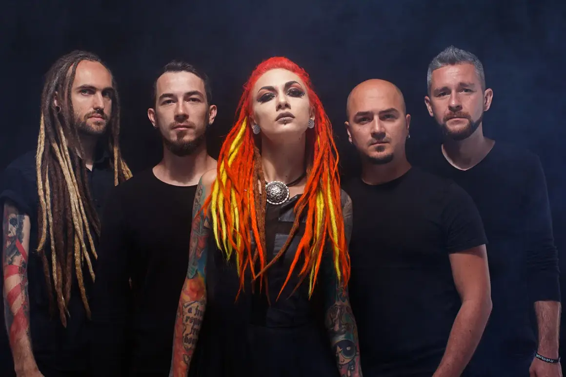 La band "Infected Rain" posa con look aggressivo. La cantante ha capelli rosso-giallo e tatuaggi colorati.