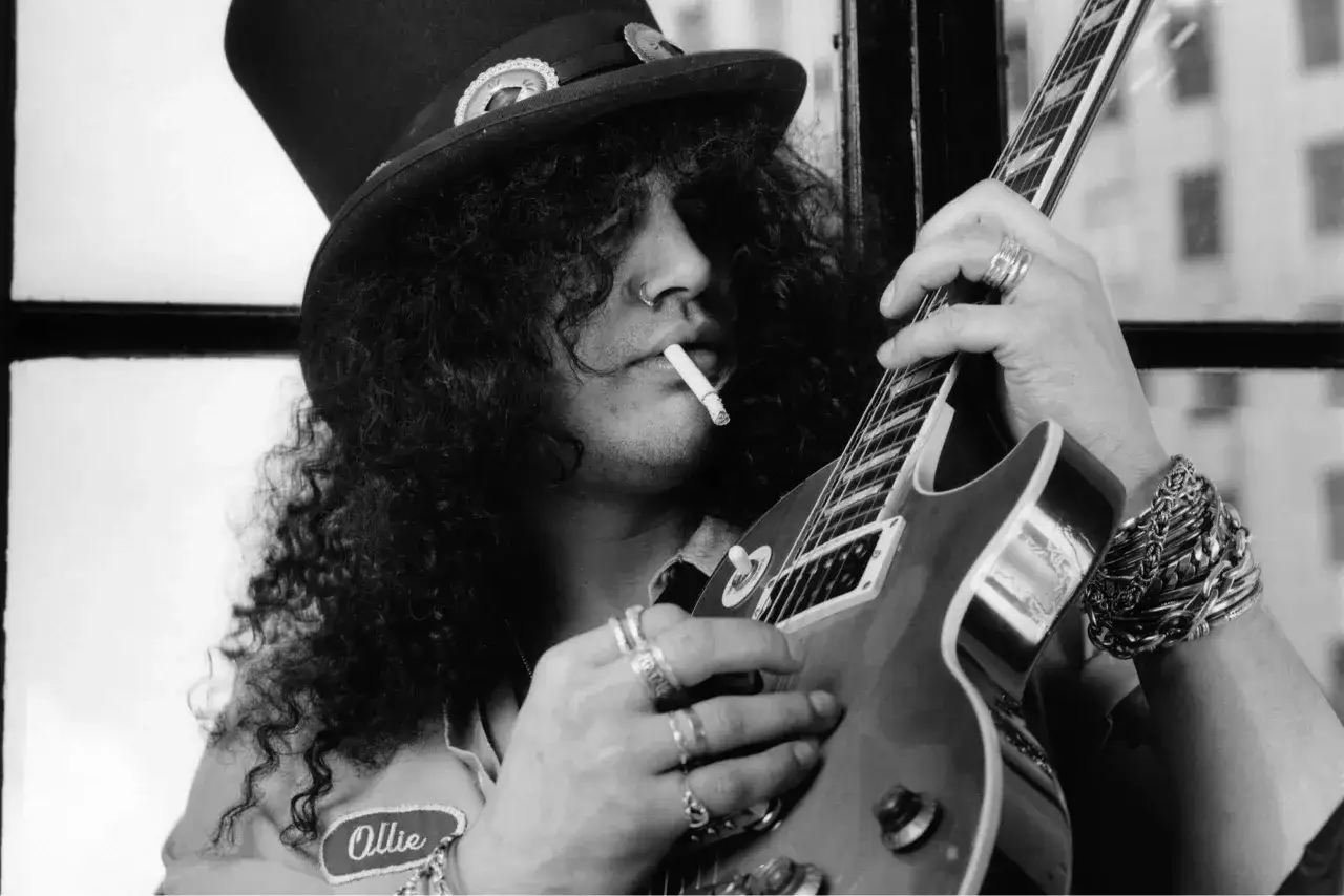 Slash con sigaretta e cappello a cilindro, chitarra in mano, icona rock degli anni 90.