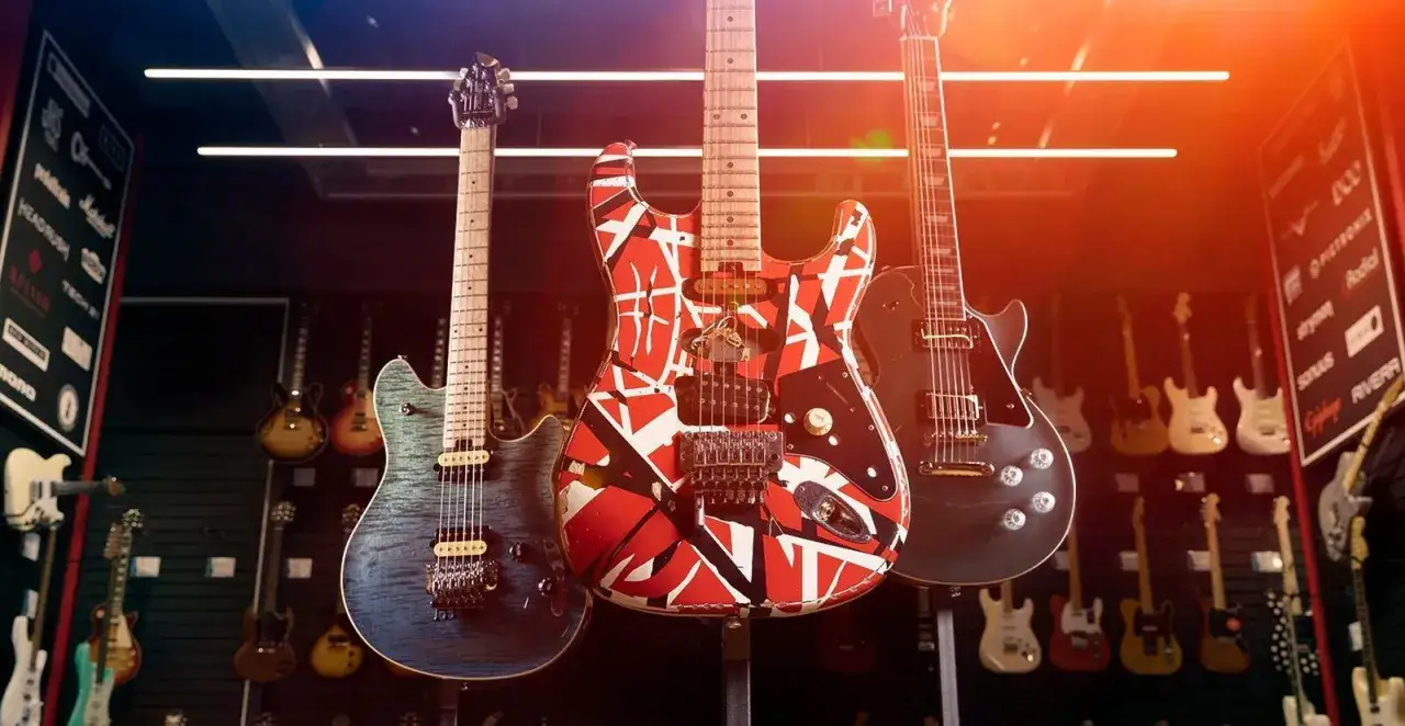 Tre chitarre iconiche: una blu fiammata, una rossa e bianca stile Van Halen e una nera Les Paul. La scelta tra Les Paul vs Stratocaster &egrave; un dilemma per ogni chitarrista.