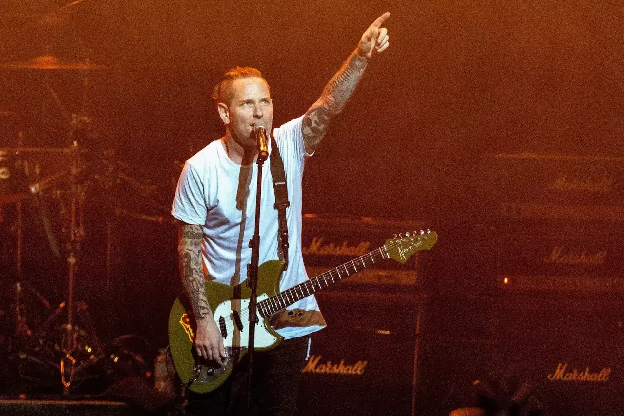 Corey Taylor, con la sua band, sul palco con chitarra e microfono, punta il dito verso l'alto.