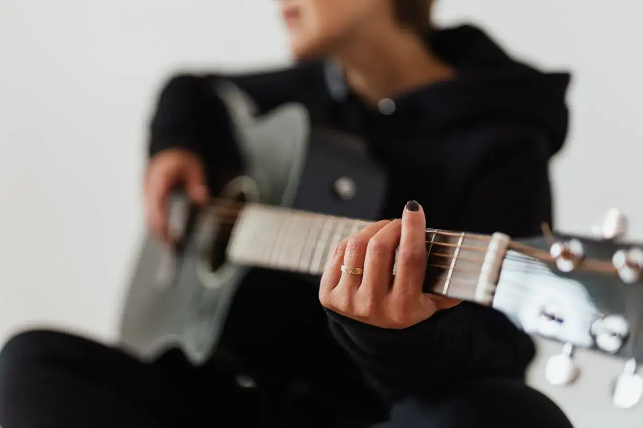 Mano che preme le corde di una chitarra acustica, imparare a suonare la chitarra è un viaggio musicale.