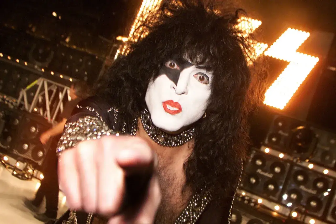 Paul Stanley dei Kiss, con il suo trucco iconico, punta il dito verso di te, pronto per un bacio rock.