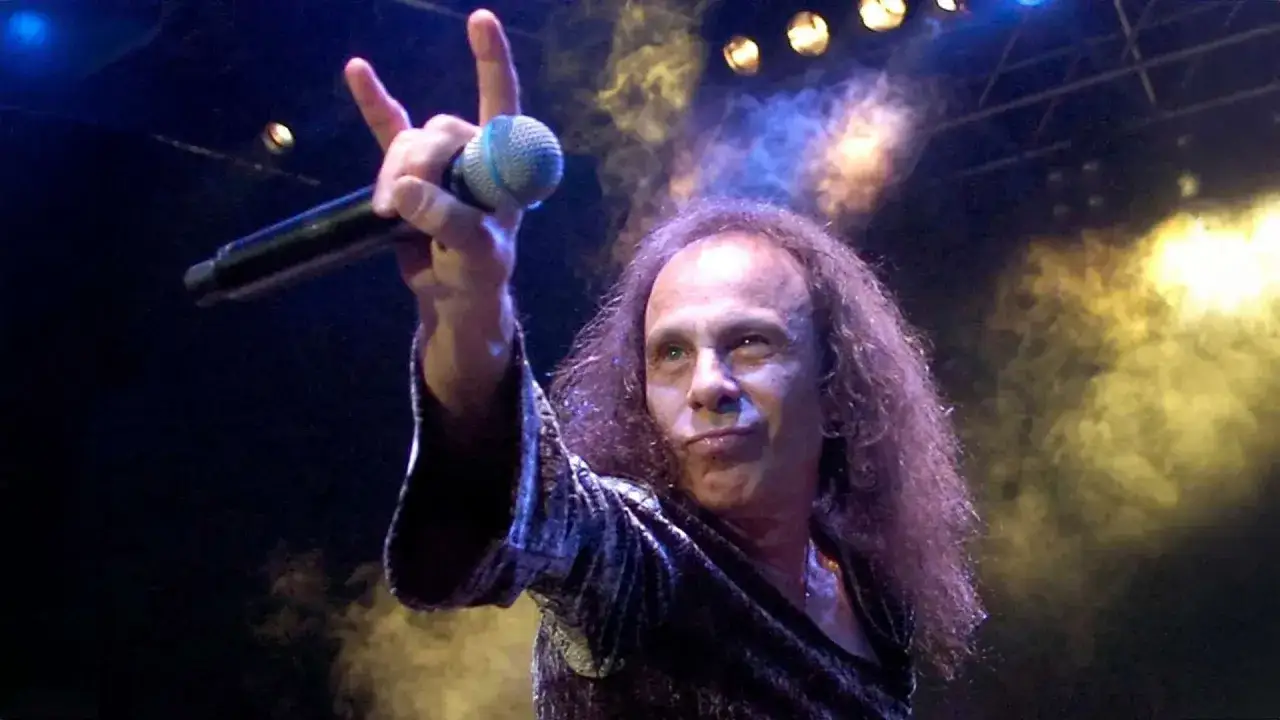 Ronnie James Dio, icona heavy metal, saluta il pubblico con il segno delle corna. La sua voce potente ha segnato generazioni, un'eredit&agrave; che sfida la morte.