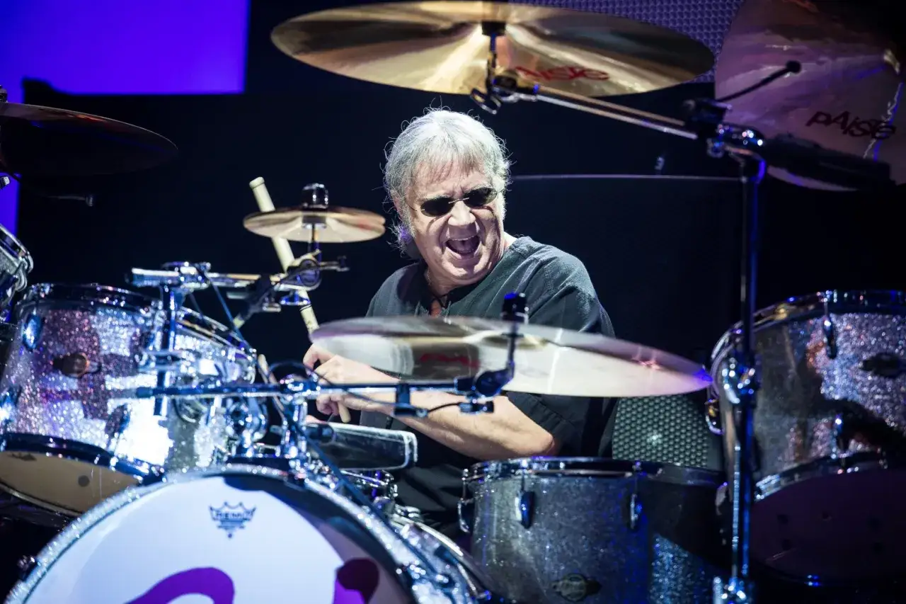 Ian Paice, batterista dei Deep Purple, suona con passione dietro la sua batteria scintillante, occhiali da sole e bocca spalancata.