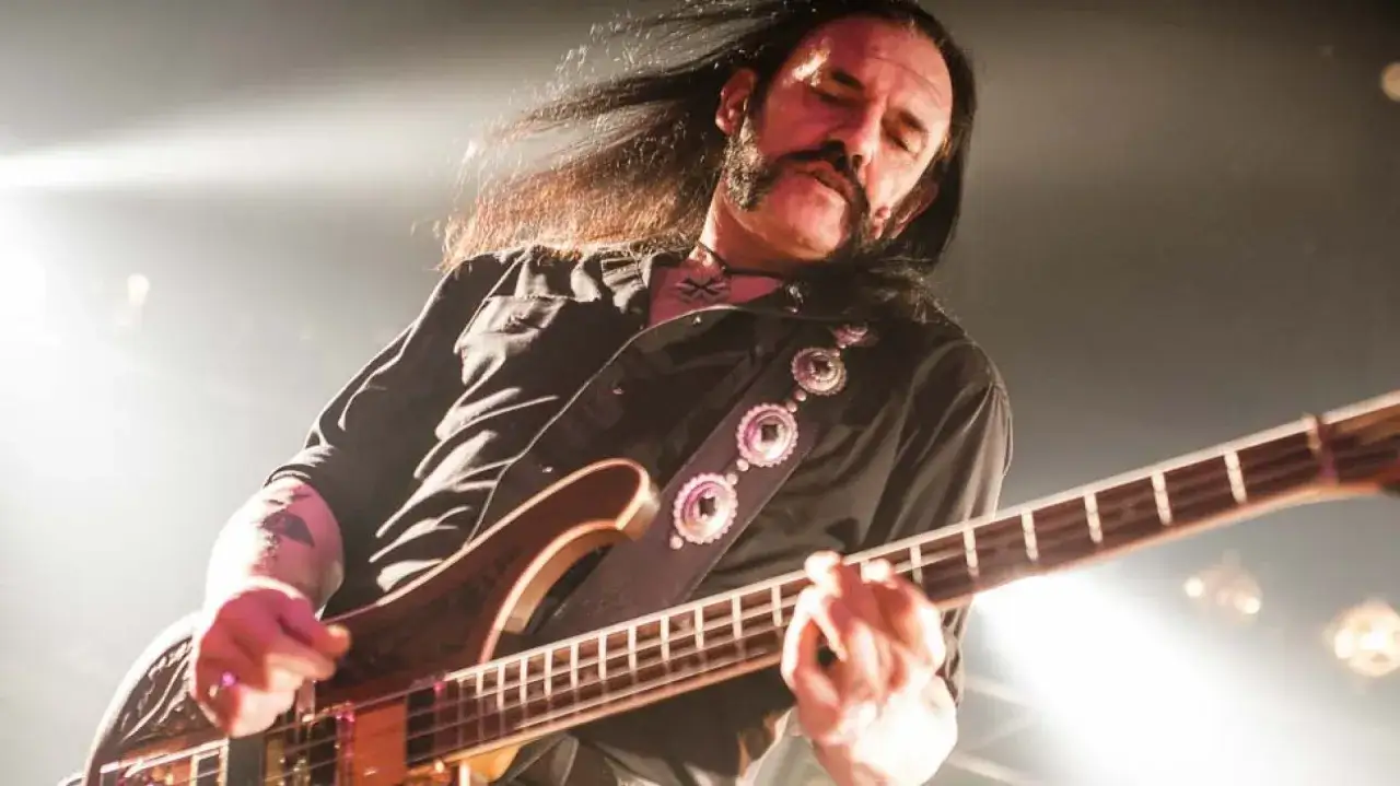 Lemmy Kilmister, icona del rock, suona il basso con passione sul palco, i capelli lunghi mossi dalla musica.