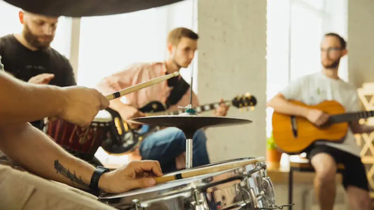 Gruppo musicale prova, con un batterista che usa bacchette, chitarristi in sottofondo. Il metronomo cos'è? Uno strumento per mantenere il tempo.