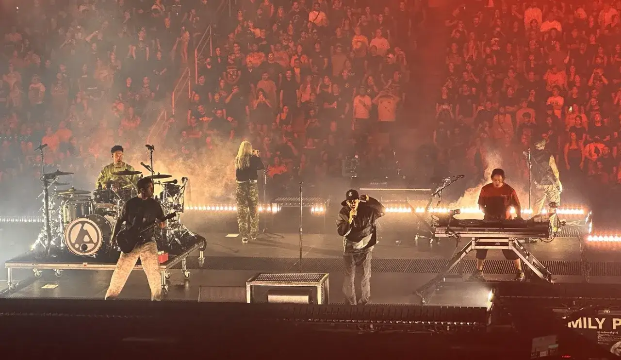 Concerto dal vivo con band che ricorda il genere Linkin Park. Sul palco, un chitarrista, un batterista, due cantanti e un tastierista, davanti a un pubblico acceso.