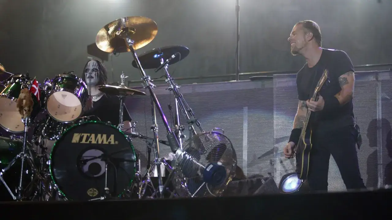 Joey Jordison, con trucco facciale e capelli lunghi, suona la batteria. Accanto a lui, un chitarrista con tatuaggi.