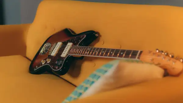 Chitarra Fender Jazzmaster color sunburst appoggiata su un divano giallo. Un duello tra jaguar e jazzmaster, quale suono preferisci?