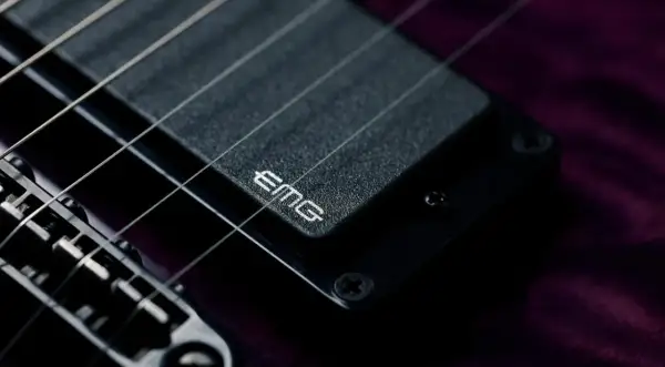 Dettaglio di una chitarra elettrica con pickup attivi EMG. Le corde metalliche brillano sopra il pickup nero.