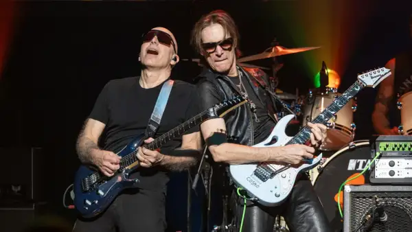 Joe Satriani e Steve Vai, due leggende della chitarra, suonano insieme sul palco. La band di Steve Vai è in piena azione.