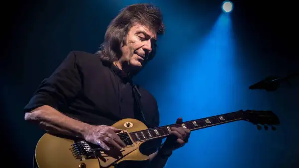 Steve Hackett, ex chitarrista dei Genesis, suona la sua chitarra dorata sotto un fascio di luce blu.