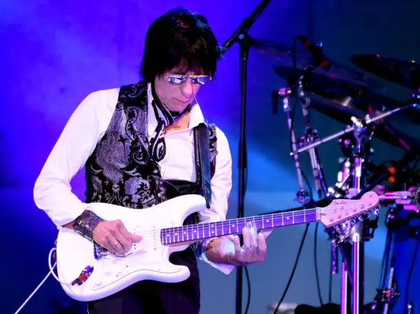 Jeff Beck, con occhiali da sole e gilet decorato, suona la sua chitarra bianca con la band.