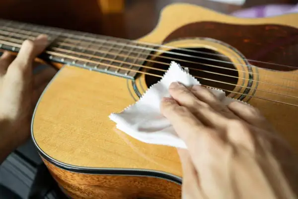 Mani che puliscono la chitarra classica con un panno bianco, un gesto essenziale per la cura dello strumento.