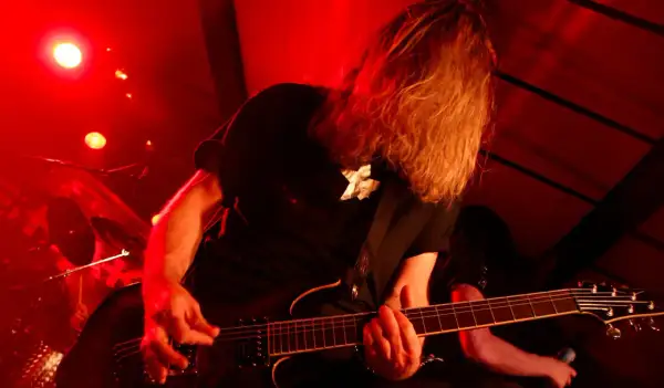 Chitarrista con lunghi capelli biondi, immerso nella luce rossa, crea la base ritmica di un brano con la sua chitarra elettrica.