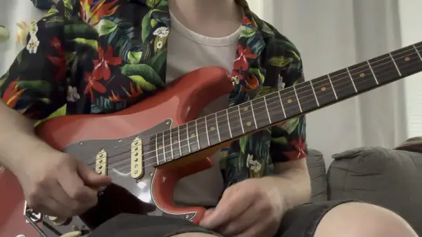 Un chitarrista con una camicia floreale suona una chitarra rossa, ricordando lo stile di Guthrie Govan.