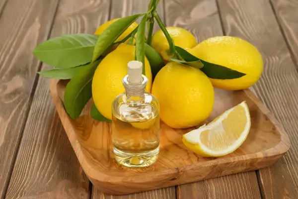 Un flacone di olio di limone chitarra, circondato da limoni freschi e foglie verdi, su un vassoio di legno.