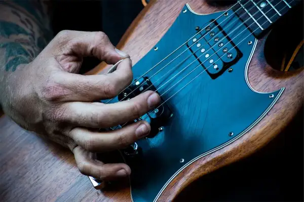 Mano che pizzica le corde di una chitarra elettrica. È più facile suonare la chitarra elettrica o acustica? La risposta è soggettiva.