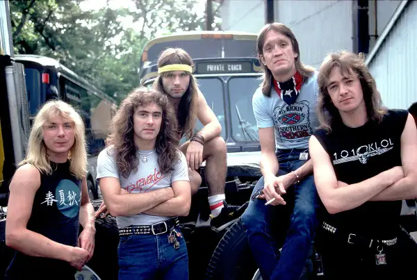 Cinque rocker con capelli lunghi e abbigliamento tipico dei gruppi metal anni 90, posano davanti a un bus privato.