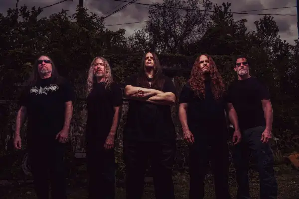 I membri dei Cannibal Corpse posano in un ambiente esterno cupo, con alberi e cielo nuvoloso sullo sfondo.